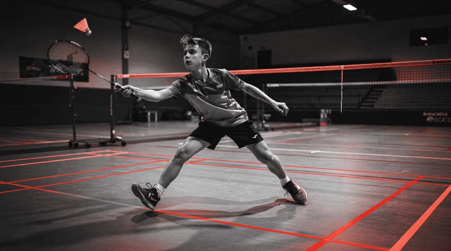 young badminton player mid-smash on an academy court